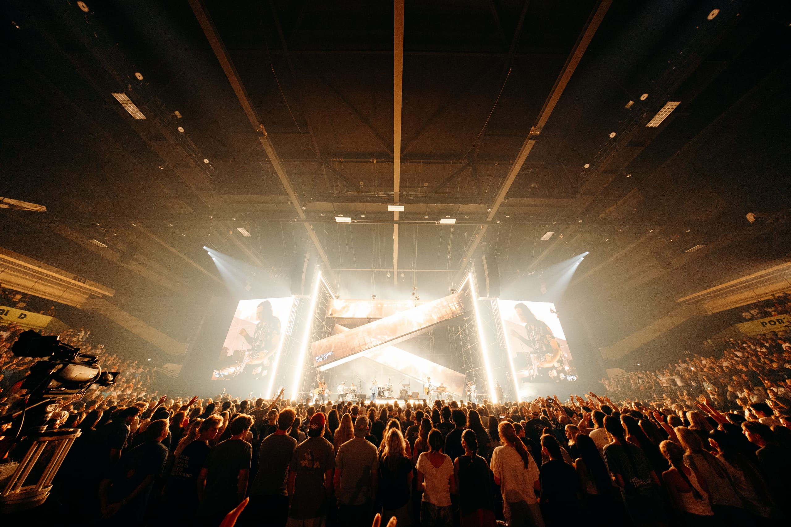 Packed arena facing a lit stage between two big screens
