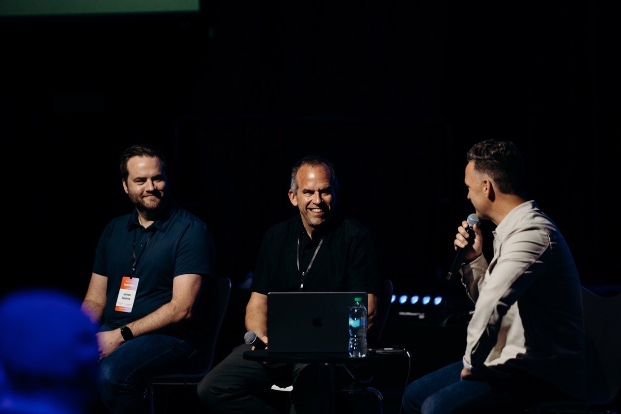Three speakers in conversation on a dark stage