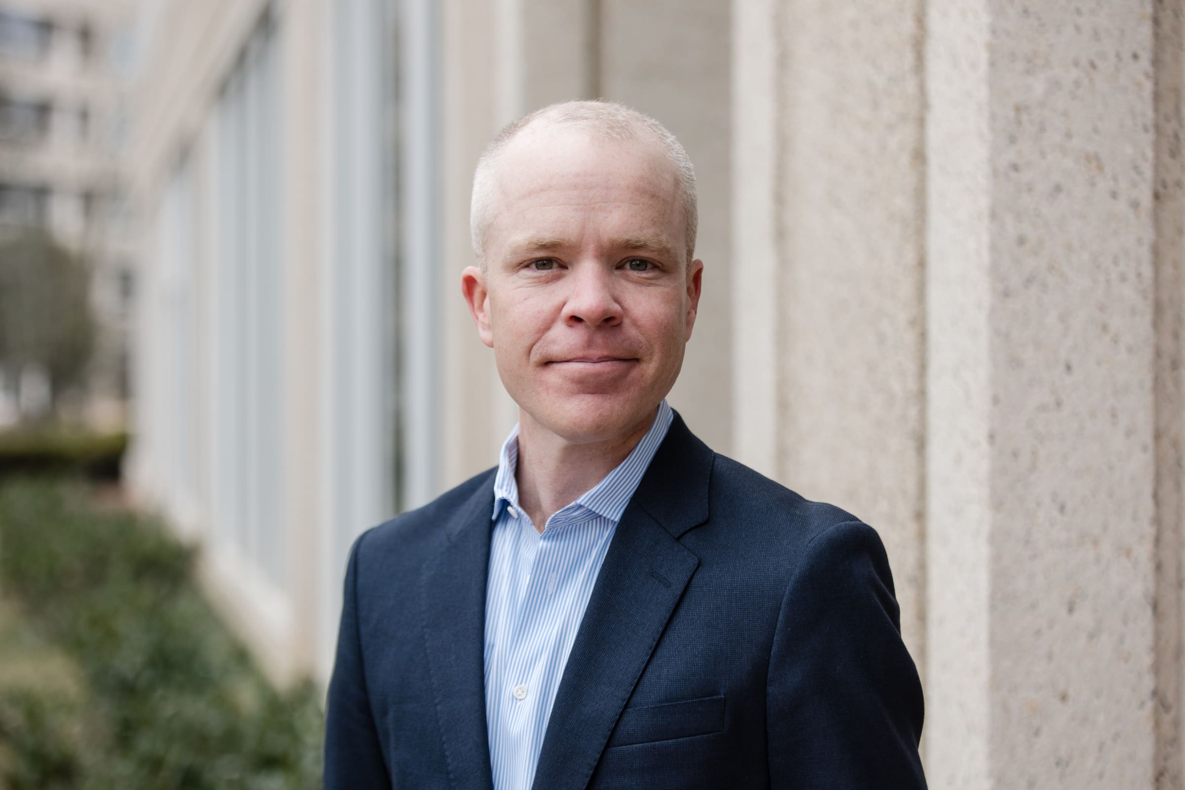 Headshot of a man in a navy blazer outside a stone building